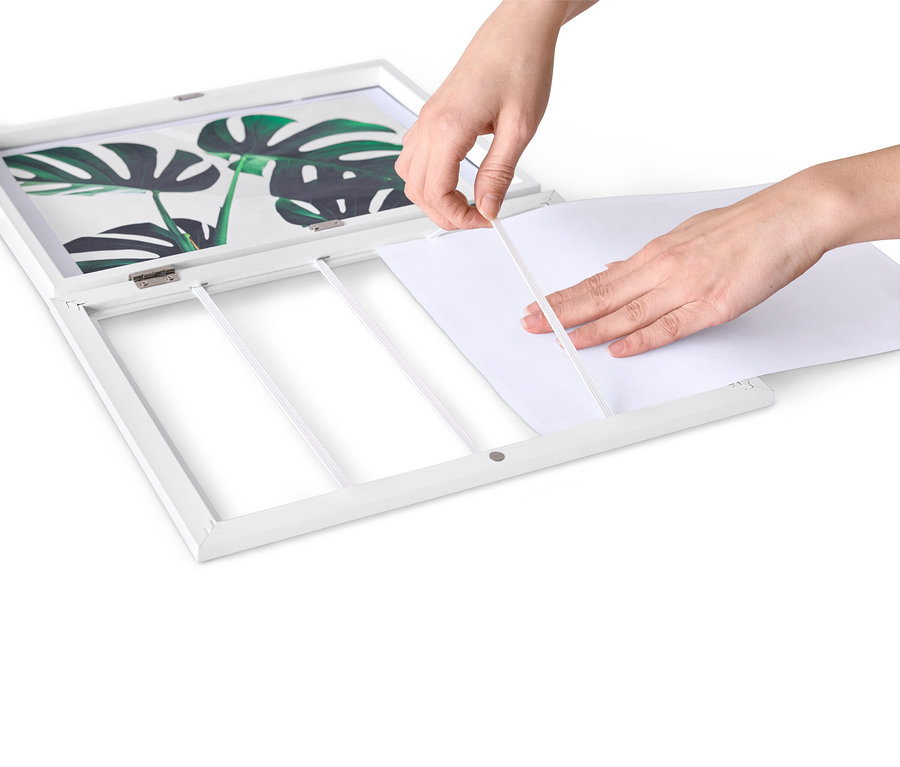 Ruky vkladajú biely papier do rozkladacieho rámčeka na obrázky.