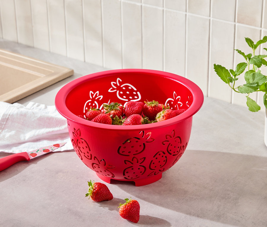 Červené sitko s motívom jahôd plné jahôd, vedľa neho leží nôž s motívom jahôd.