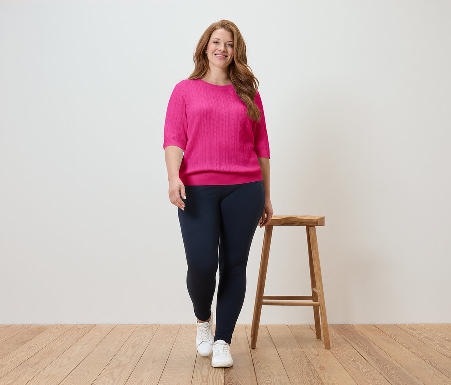 Žena kráča v ružovom tope a tmavomodrých legínach na drevenej podlahe