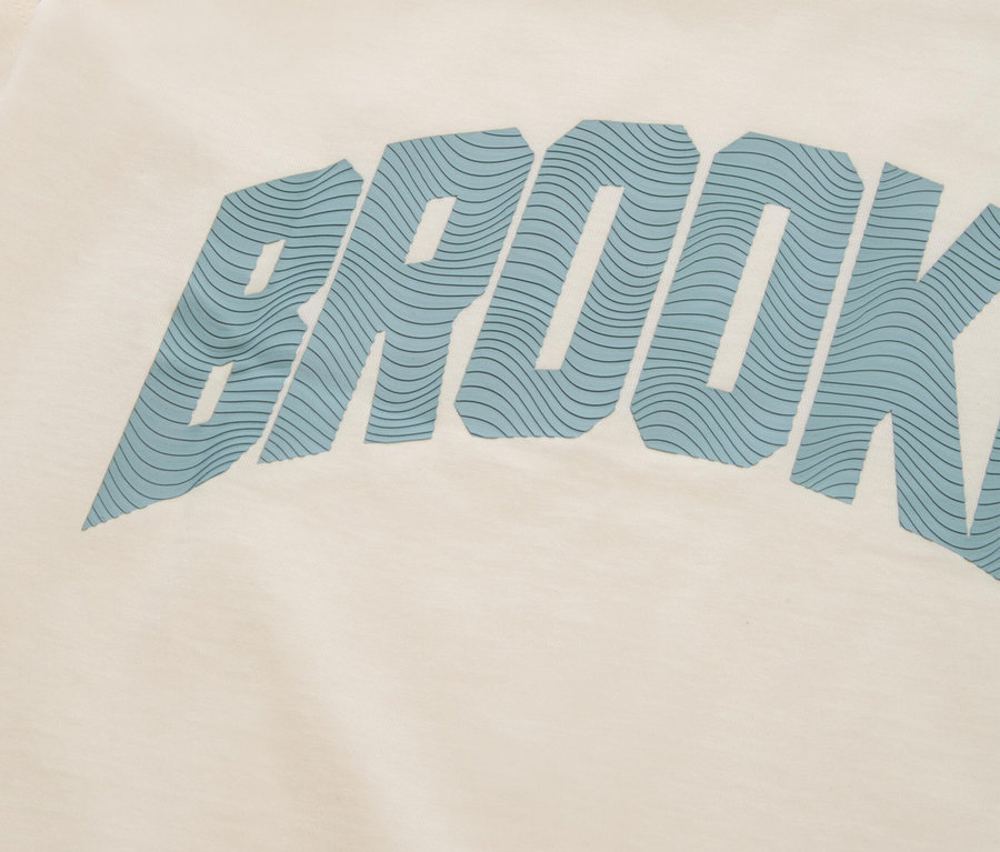 Detailný záber krémového trička s modrým nápisom „BROOKLYN“.