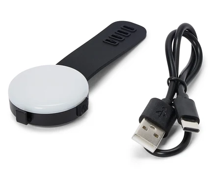 Na bielom pozadí leží čierne, okrúhle LED svetlo s čiernou rukoväťou a USB káblom.