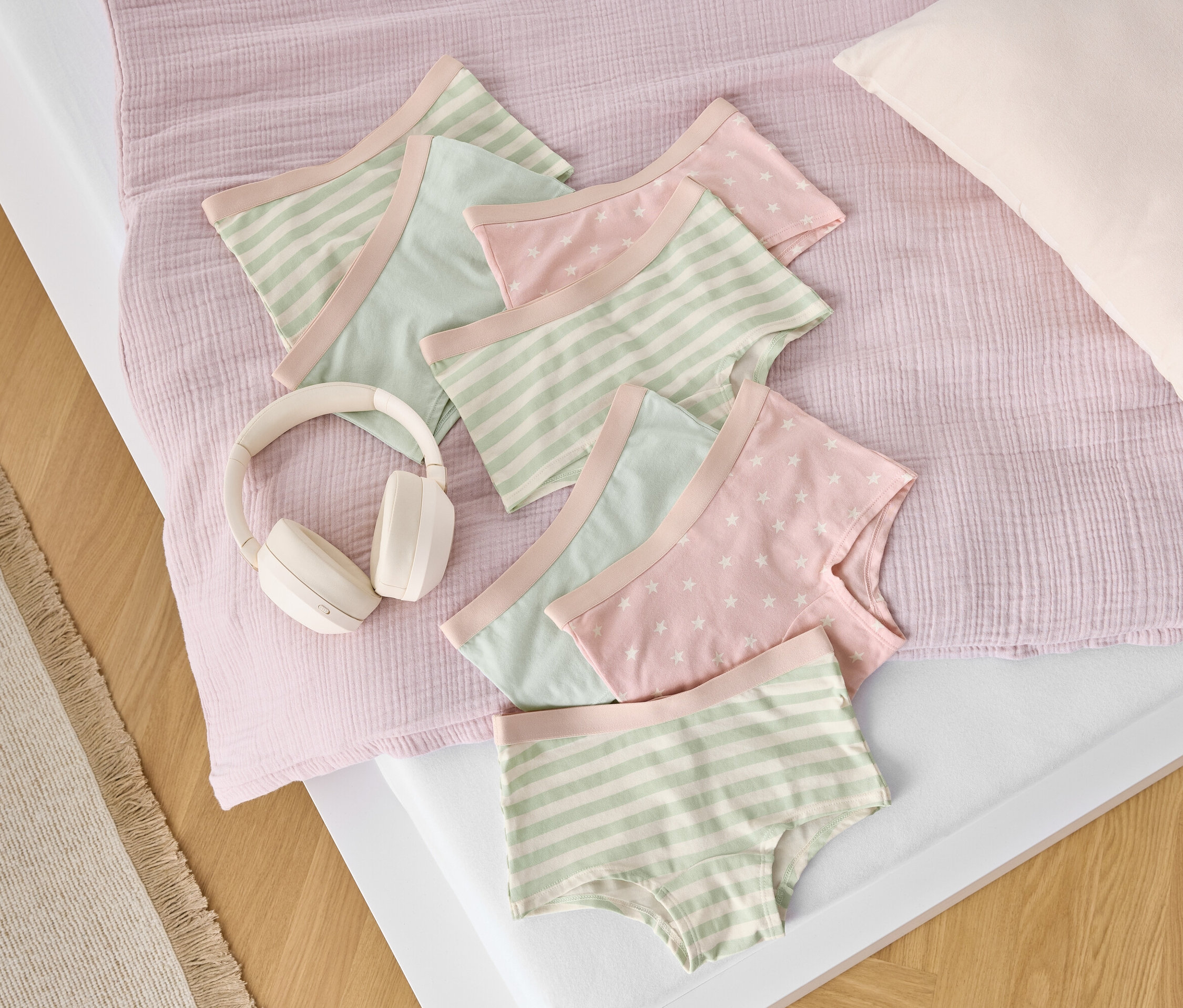 Na posteli ležia bavlnené slipy s pruhmi a hviezdami vedľa bielych slúchadiel.