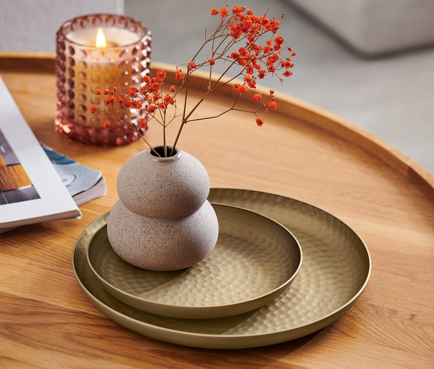 Na drevenom stolíku ležia dva dekoratívne podnosy, váza s kvetmi a sviečka.