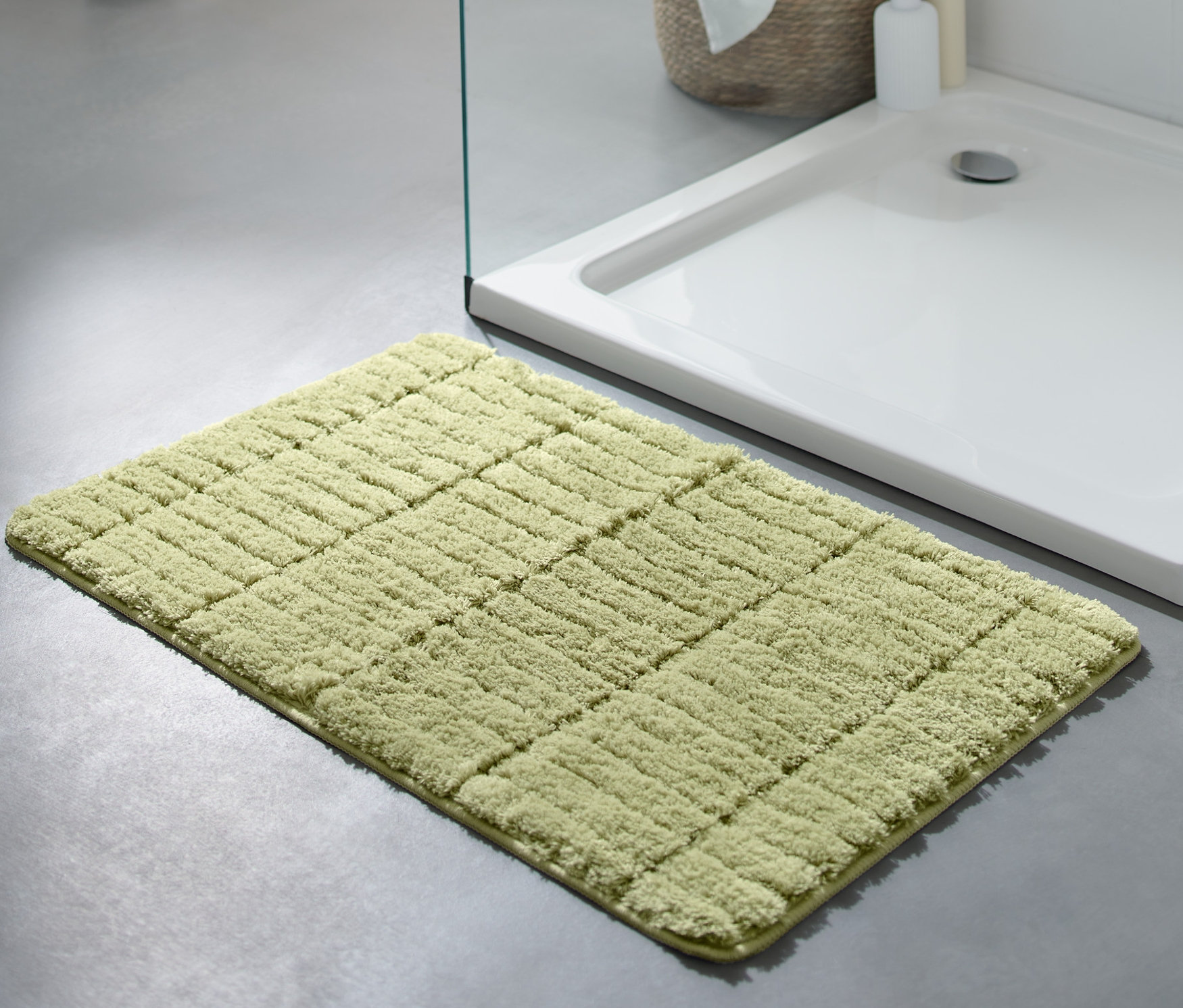 Zelená predložka do kúpeľne Comfort, cca 50 x 80 cm, leží na sivej podlahe vedľa sprchovacieho kúta.
