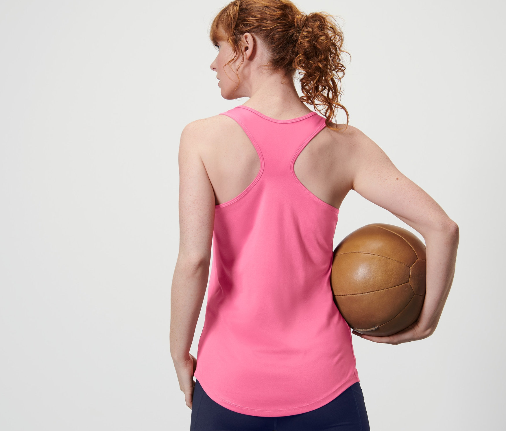 Žena zozadu drží hnedú loptu a má na sebe ružový funkčný top z 2 ks súpravy.