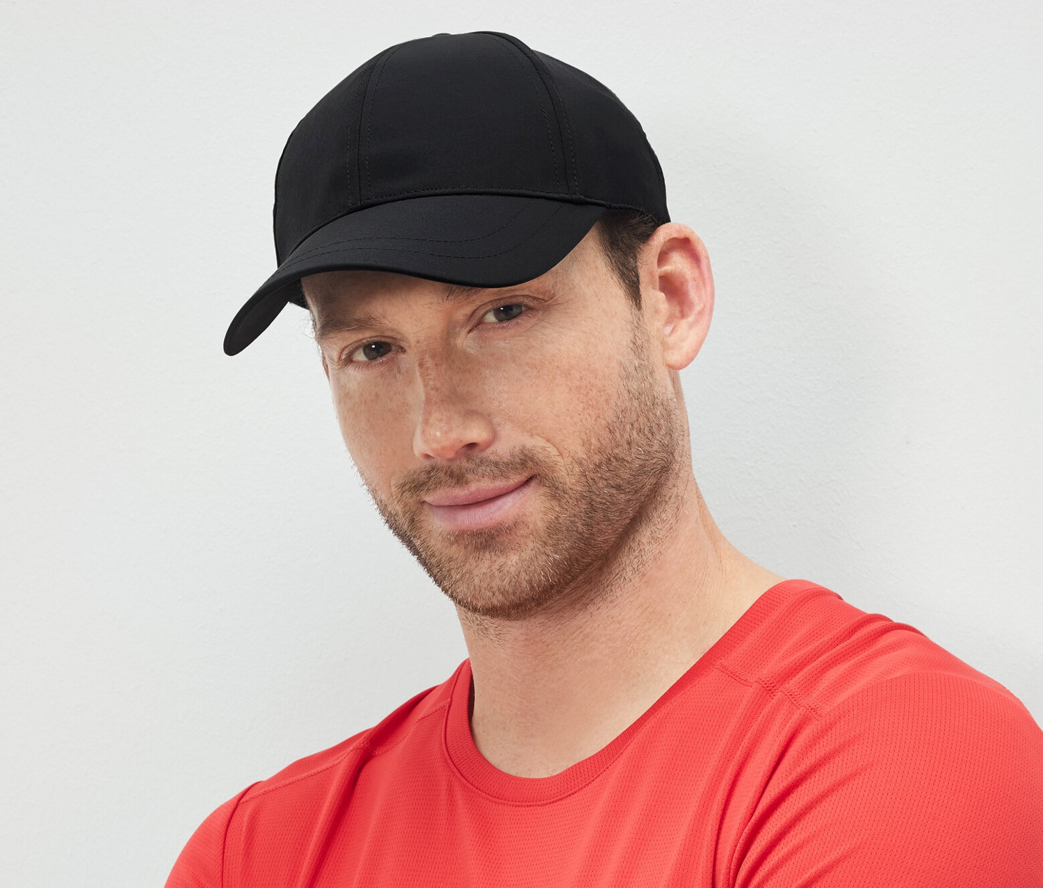 Muž so skríženými rukami nosí čiernu športovú šiltovku.