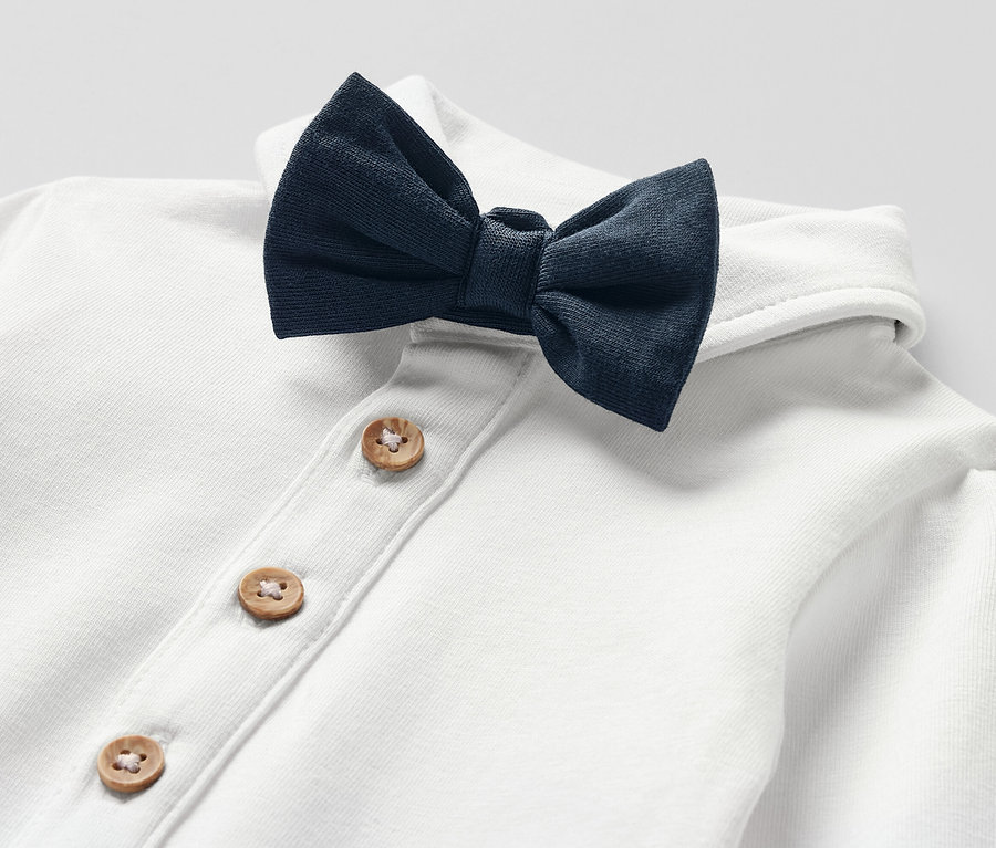 Detail bieleho detského body s motýlikom a zapínaním na drevené gombíky.