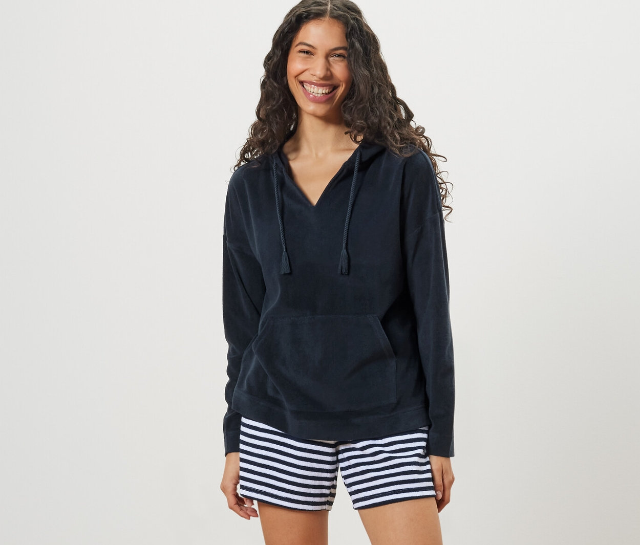 Žena má na sebe froté mikinu s kapucňou a pruhované šortky.