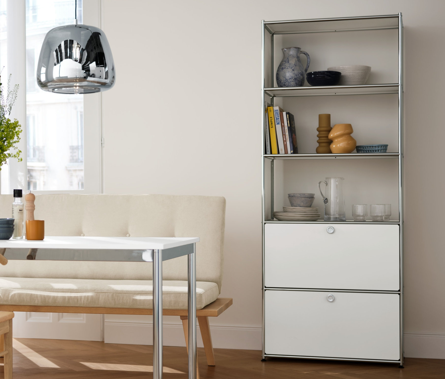 Interiér jedálne s chrómovým závesným svietidlom, kovovým stolom, regálom so zásuvkami a jedálenskými stoličkami.