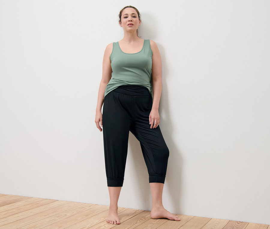 Žena pózuje v zelenom tielku a čiernych 3/4 nohaviciach na jogu.