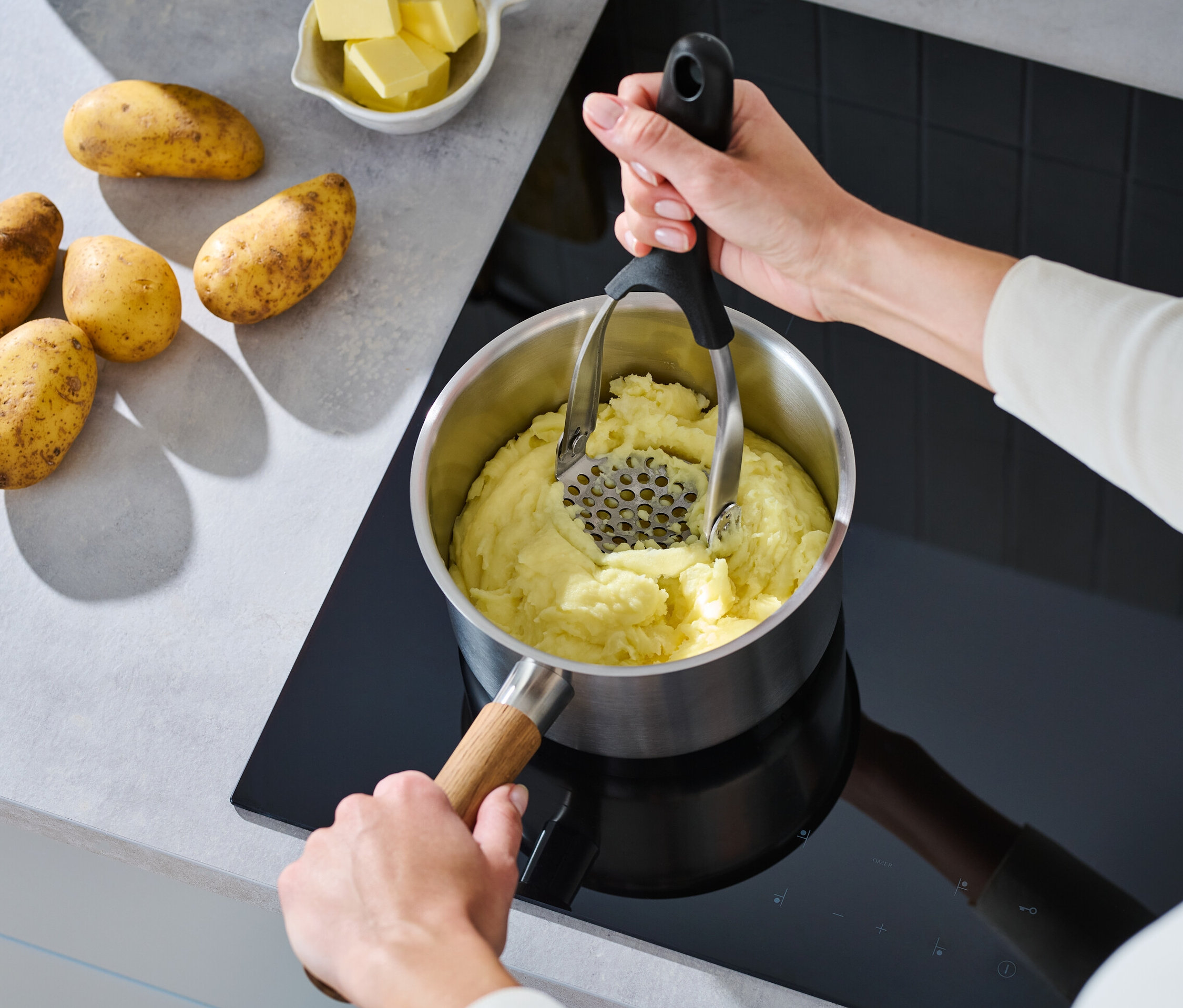 Žena pučí zemiaky pomocou skladacieho pučidla na zemiaky v hrnci na sporáku.