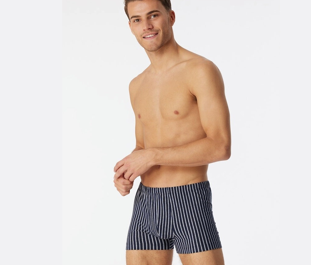 Muž s odhalenou hornou polovicou tela má na sebe tmavomodré boxerky SCHIESSER s biobavlnou.