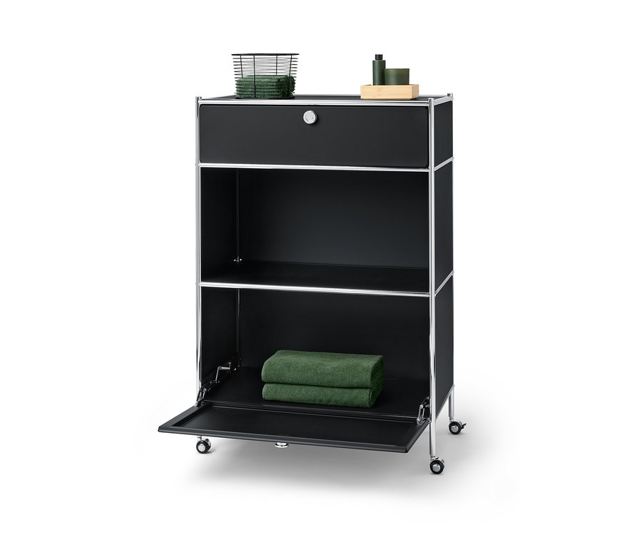 Čierna kovová komoda »CN3« s jednou zásuvkou hore, na ktorej leží košík s uterákmi, a jedným výklopným priečinkom dole, na ktorom ležia dva uteráky.