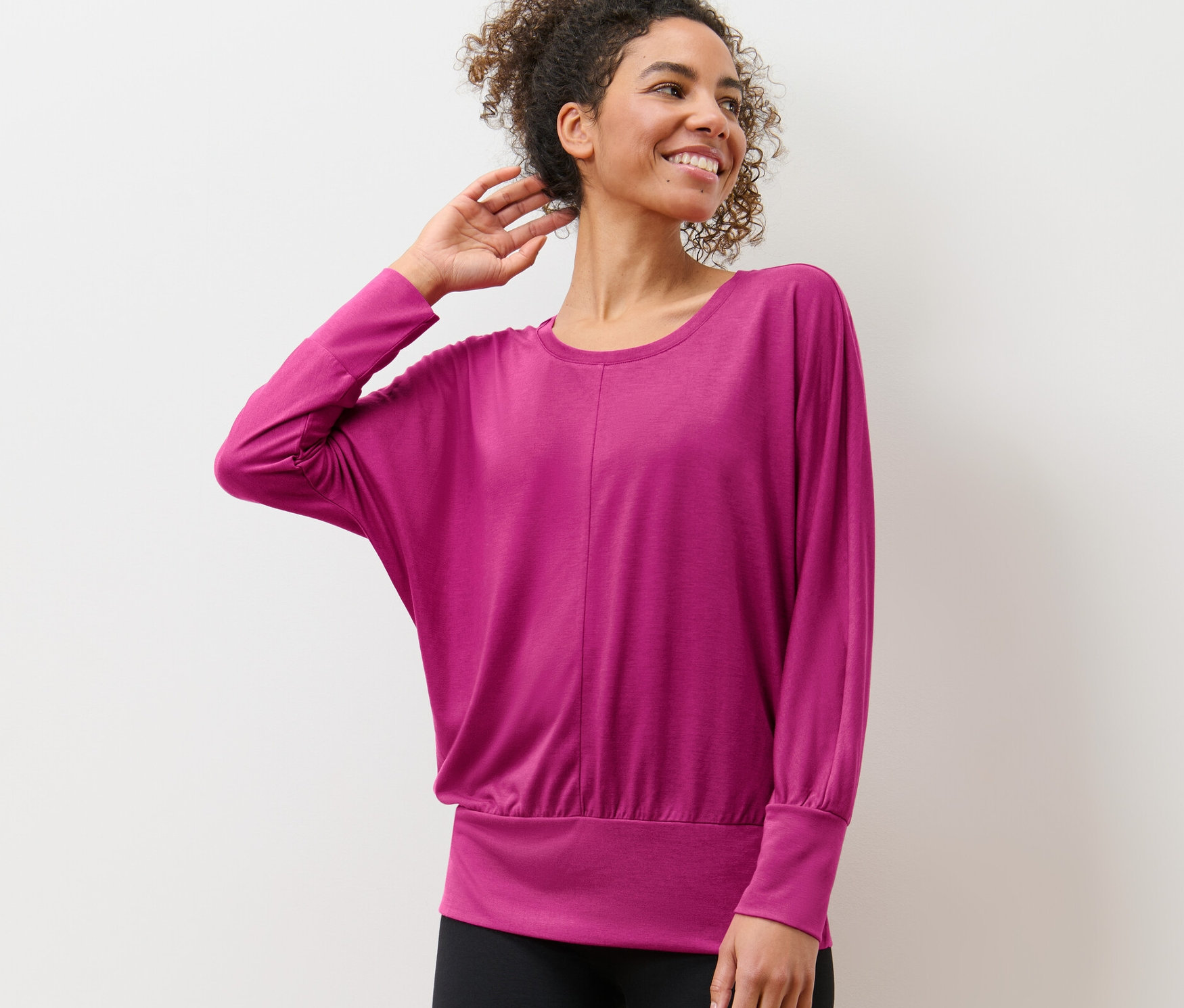 Žena v tričku na jogu pózuje pred bielou stenou.