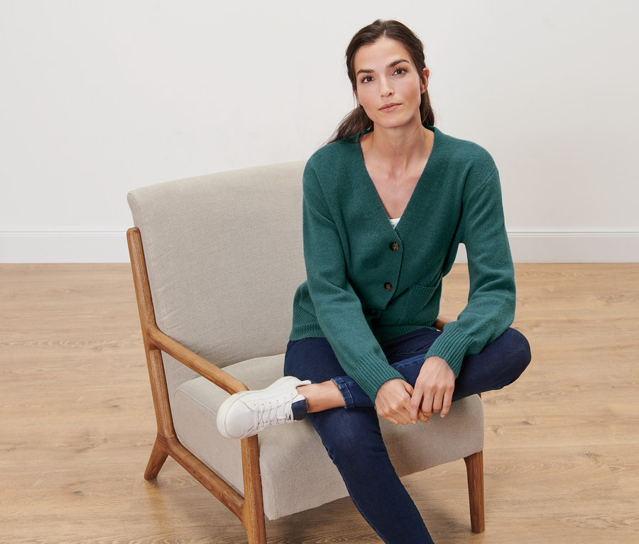 Žena sedí v kresle a má na sebe tmavozelený pletený sveter s vlnou.