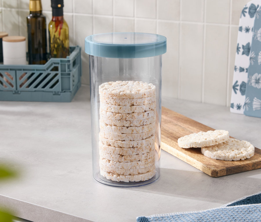 V dóze s modrým viečkom je naskladaných niekoľko ryžových koláčikov, dva ďalšie ležia na drevenej doske.