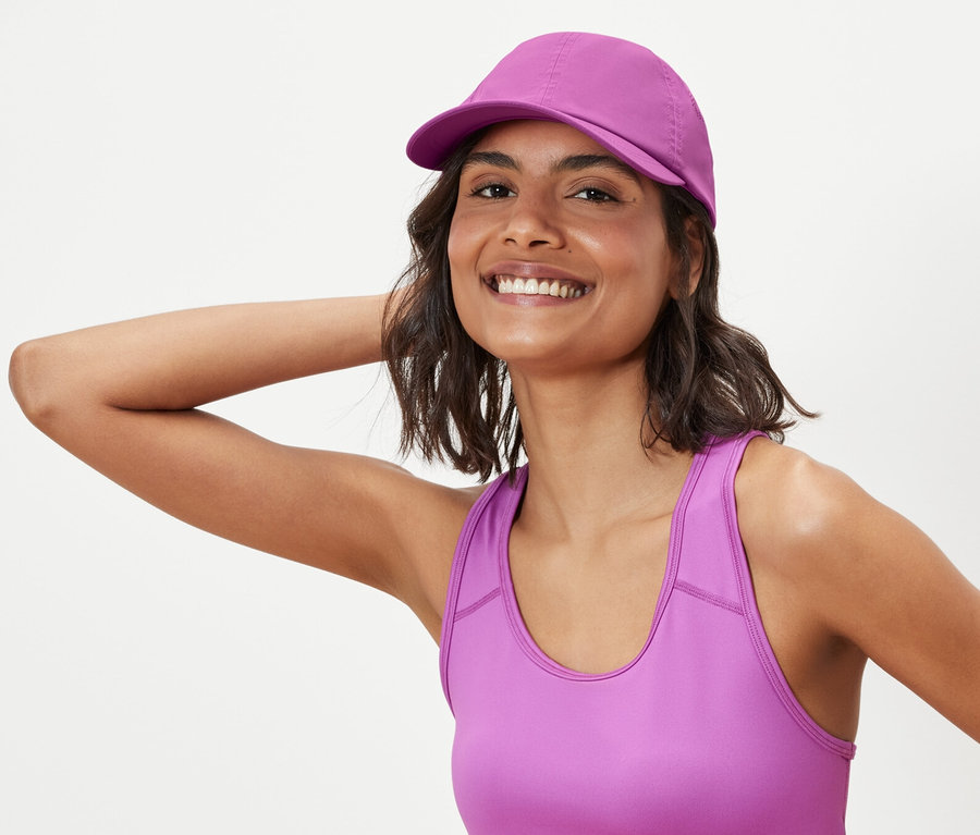 Žena pózuje v športovej podprsenke a športovej šiltovke.