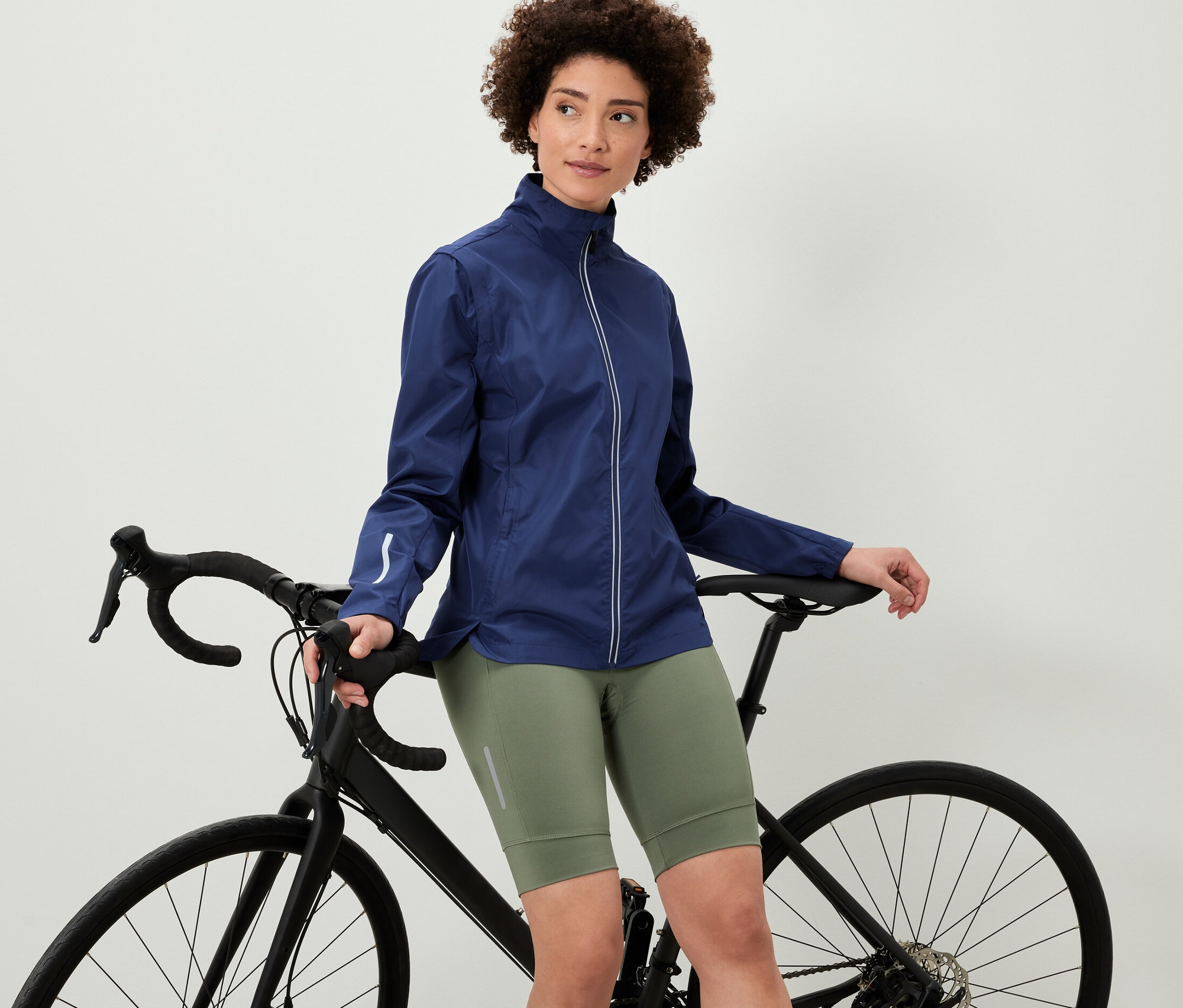 Žena opierajúca sa o bicykel má na sebe cyklistickú bundu 2 v 1.