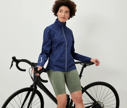 Žena opierajúca sa o bicykel má na sebe cyklistickú bundu 2 v 1.