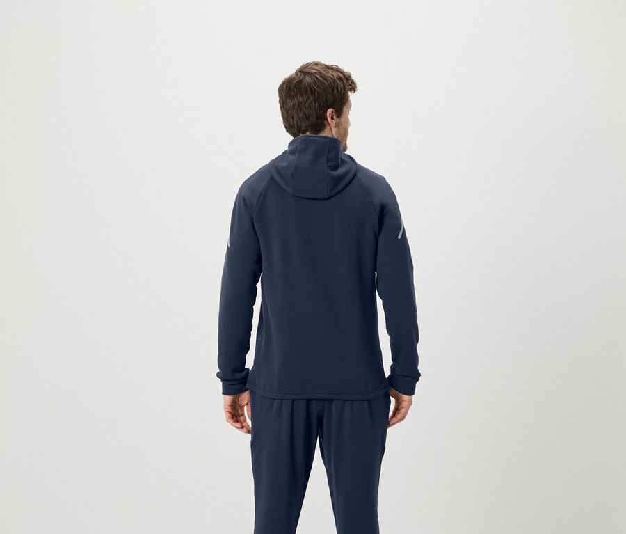 Muž chrbtom k fotoaparátu má na sebe tmavomodrú mikinu s kapucňou a tepláky.