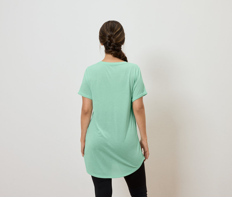 Žena chrbtom ku kamere má na sebe zelené tričko a čierne legíny.