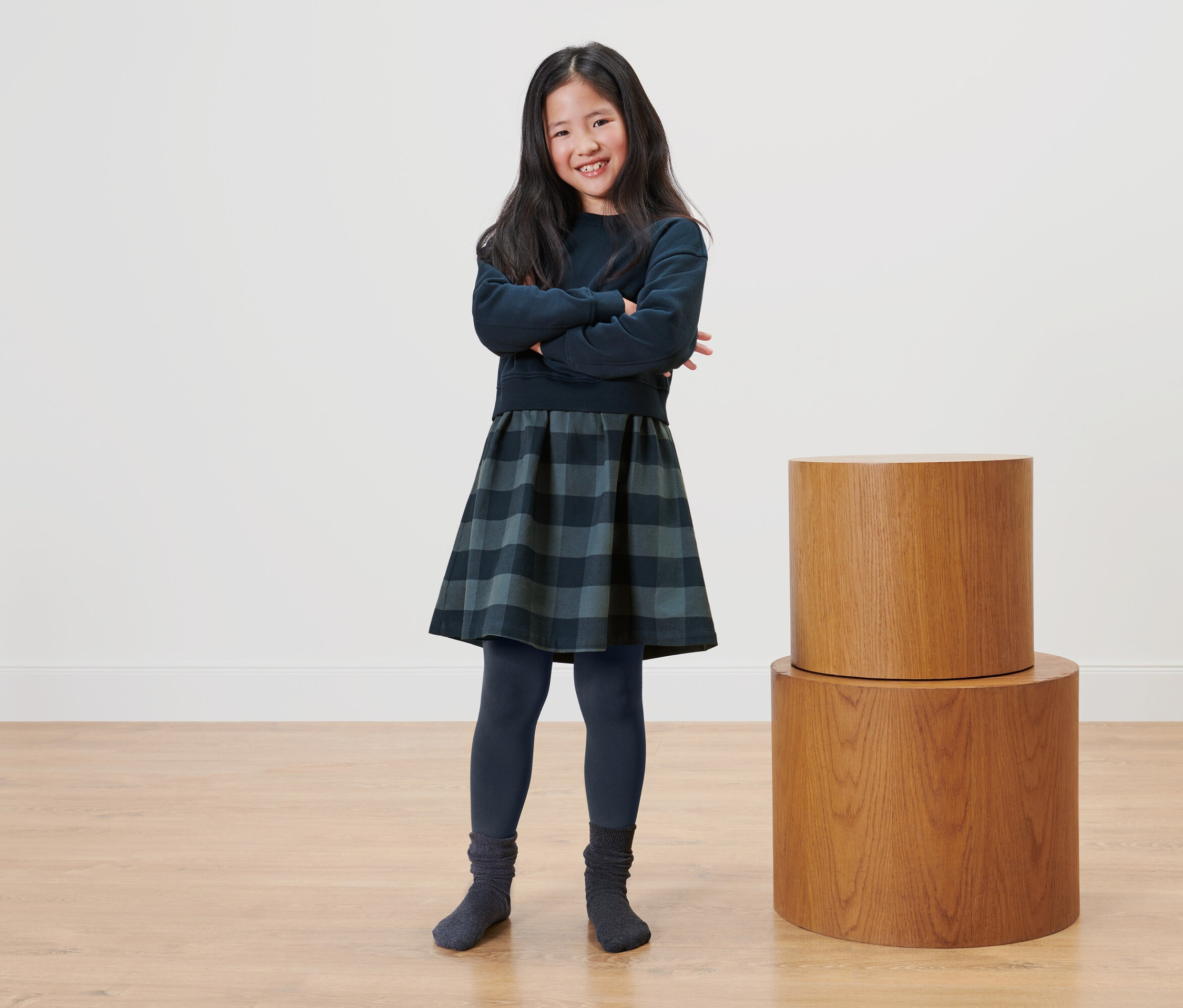 Dievča stojí so skríženými rukami vedľa dvoch drevených stolíkov.