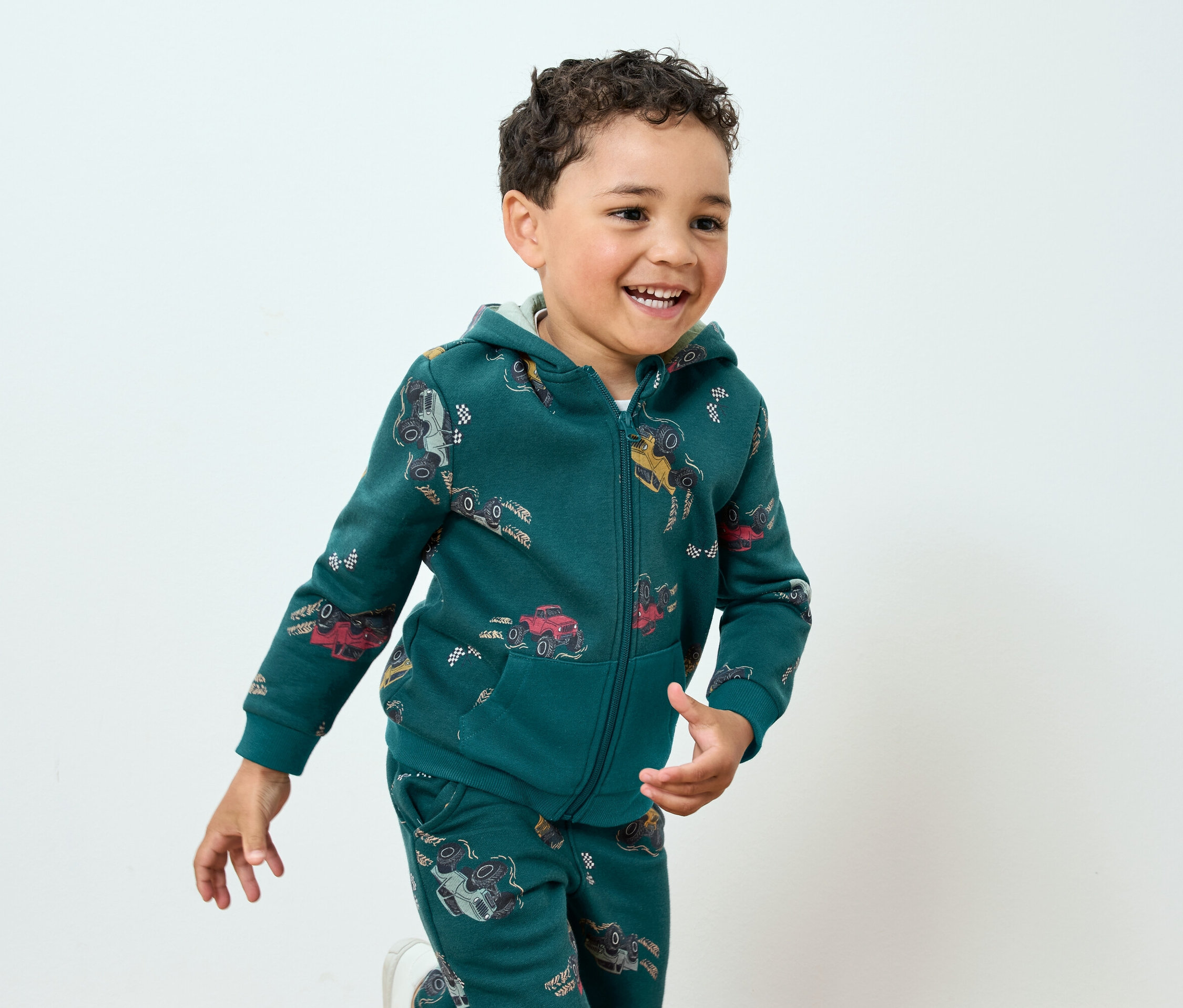 Usmievajúci sa chlapec v zelenej teplákovej súprave s potlačou áut
