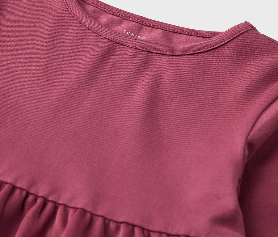 Detail ružových šiat s naberanou sukňou a okrúhlym výstrihom.