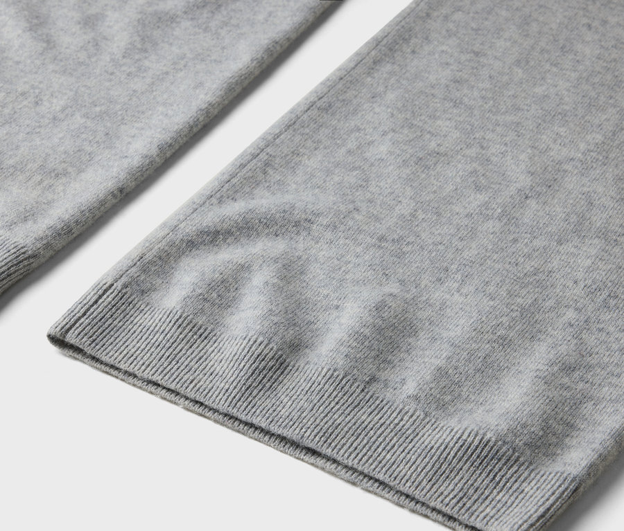 Detail šedej pletenej látky s rebrovaným lemom.