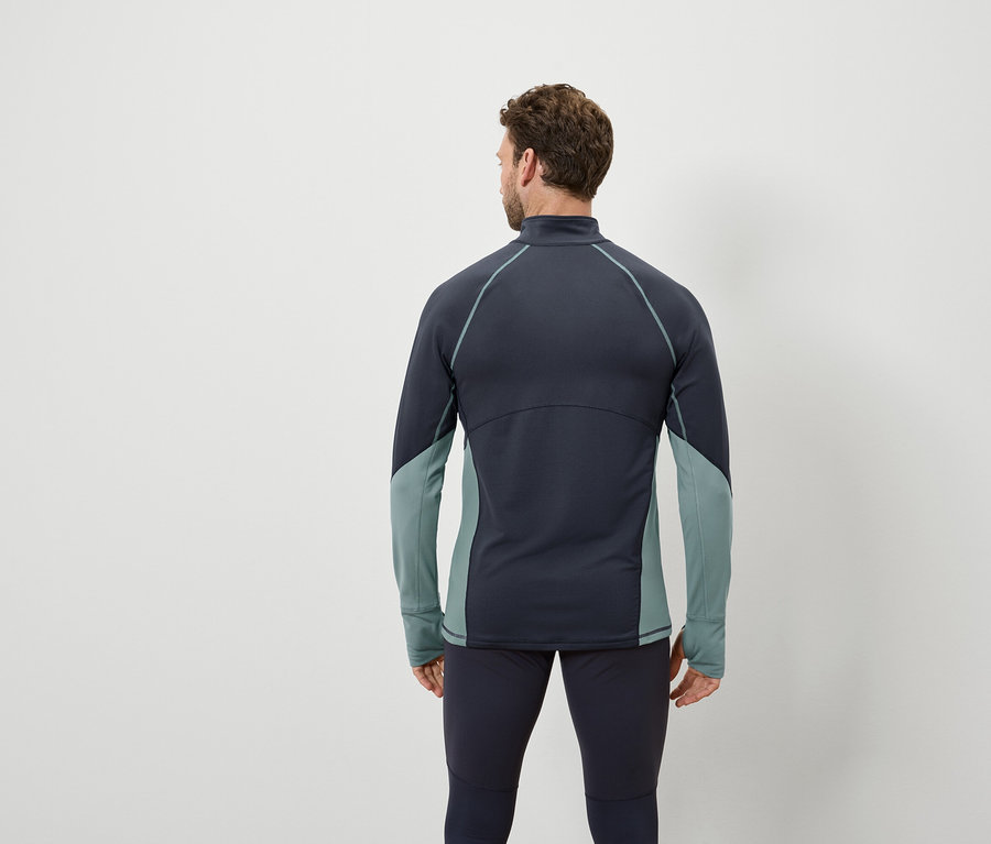 Muž chrbtom k fotoaparátu má na sebe tmavomodrý top s dlhým rukávom a sivozelenými panelmi a tmavomodré legíny.