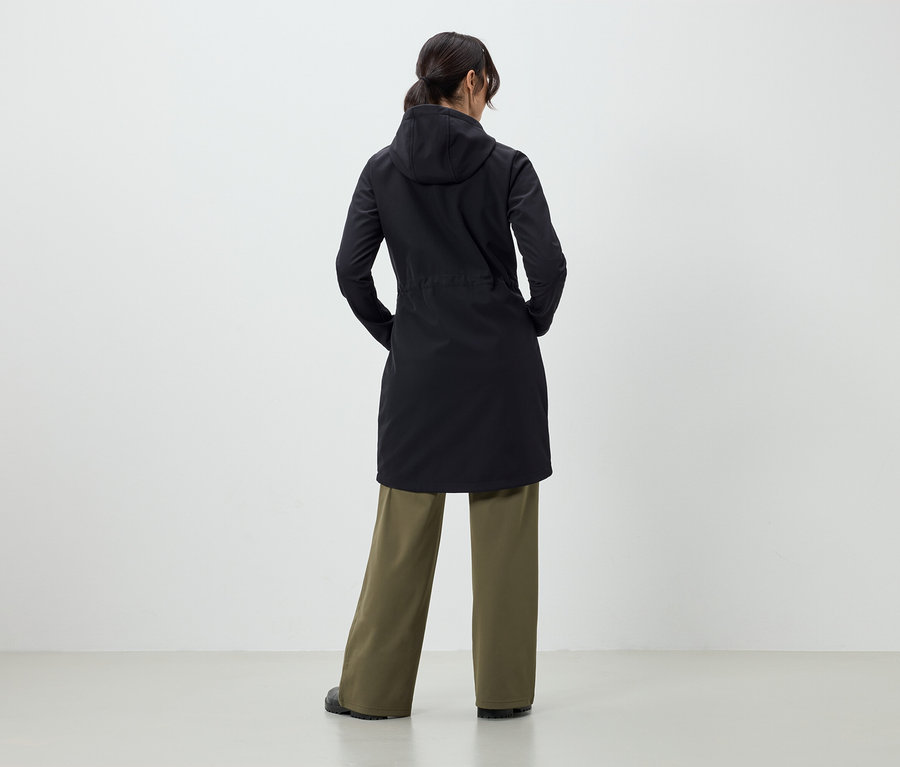 Žena chrbtom k fotoaparátu má na sebe čierny kabát a zelené nohavice.