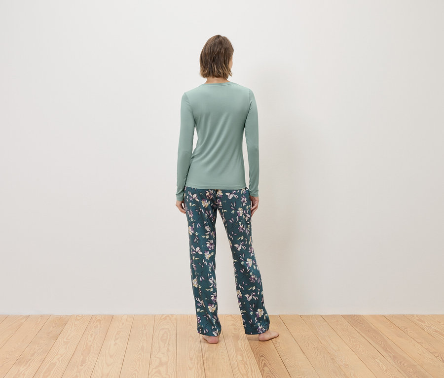 Pohľad zozadu na ženu v mätovo zelenom tričku s dlhým rukávom a tmavozelených kvetinových nohaviciach.