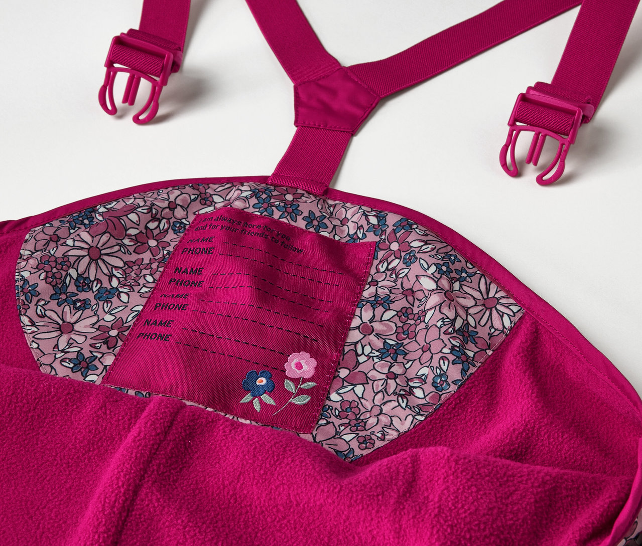 Detail detských termo nohavíc do dažďa s kvetinovou potlačou, vrátane detailov ako sú traky a štítok na meno.