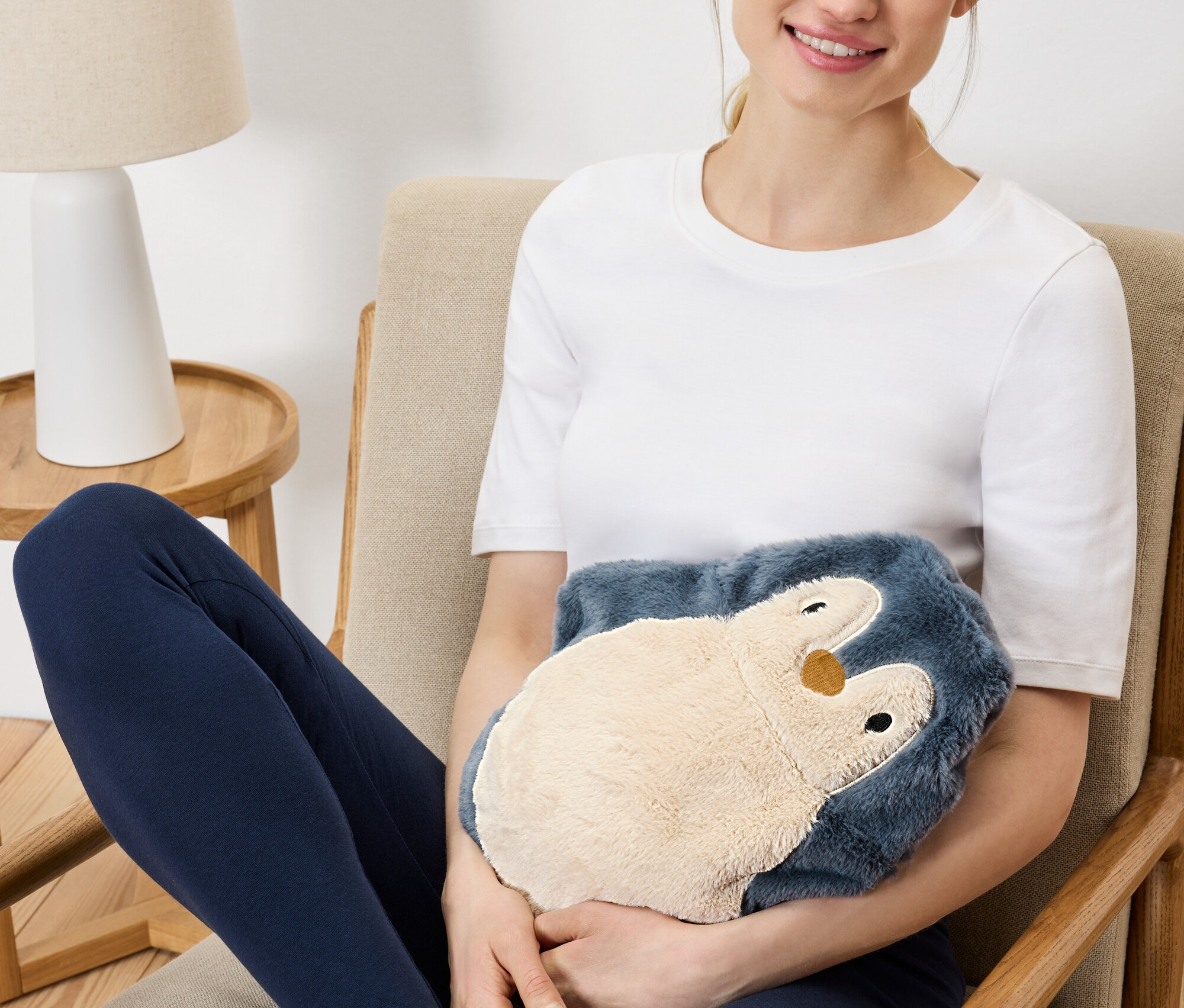 Žena sedí v kresle a drží plyšového hrejivého tučniaka.