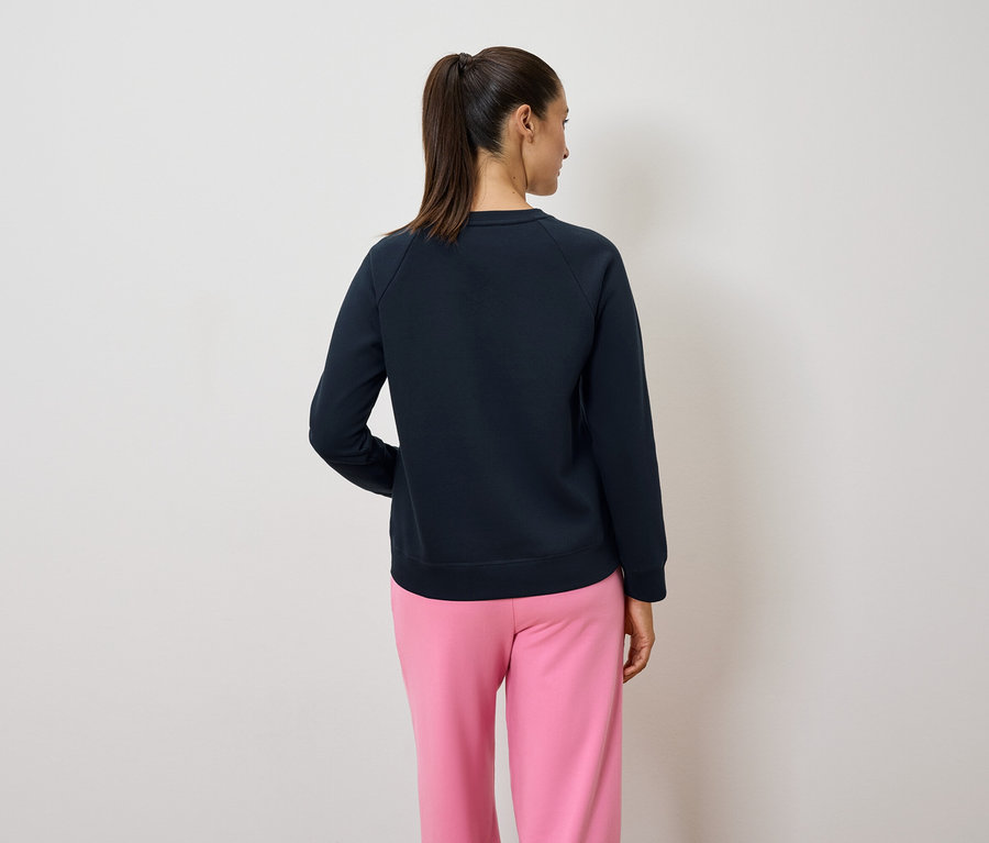 Zozadu je vidieť žena s chvostom, oblečená do tmavomodrej mikiny a ružových nohavíc.