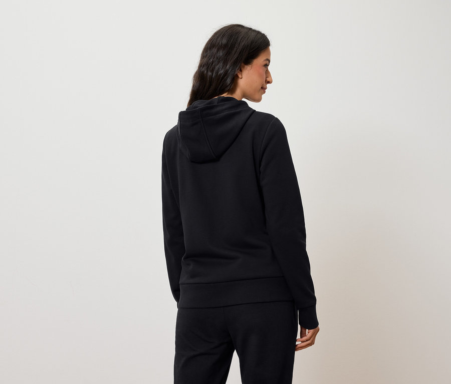 Žena z pohľadu zozadu má na sebe čiernu mikinu s kapucňou a čierne nohavice.