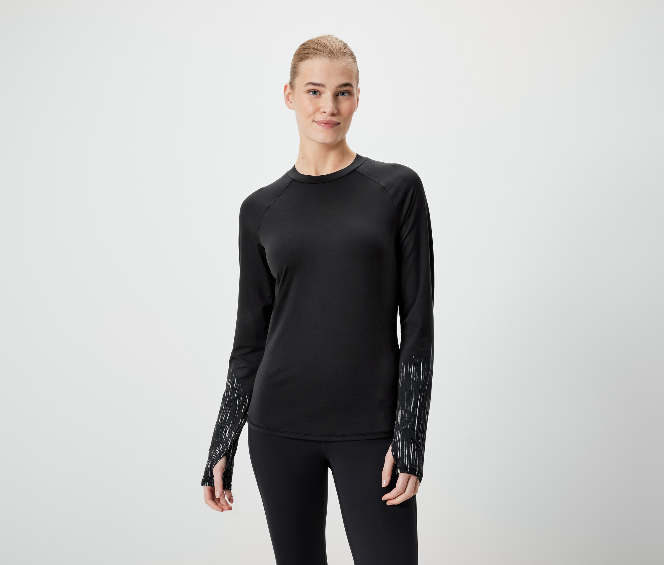Žena má na sebe čierne tričko s dlhým rukávom a čierne legíny.