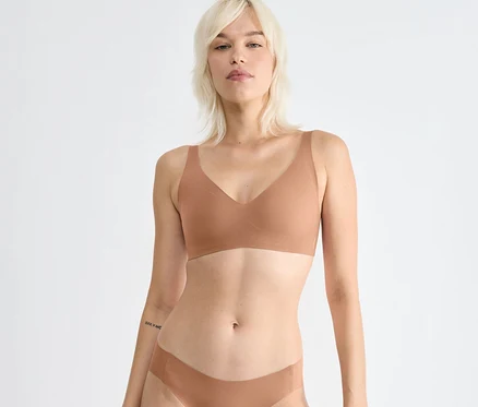 Blondínka má na sebe sloggi ZERO Feel 2.0 Soft Bra vo farbe nostalgic brown a zodpovedajúcu spodnú bielizeň, pozerá dopredu. Má tetovanie na ľavom predlaktí.