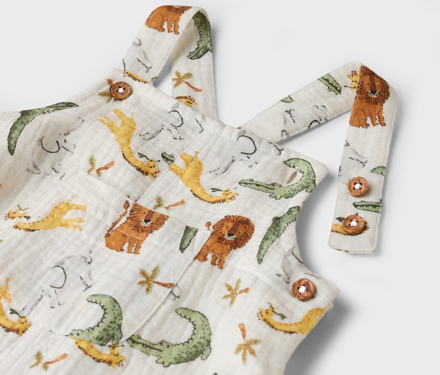 Detailný záber na biele detské montérky so vzorom krokodílov, levov, slonov a žiráf.