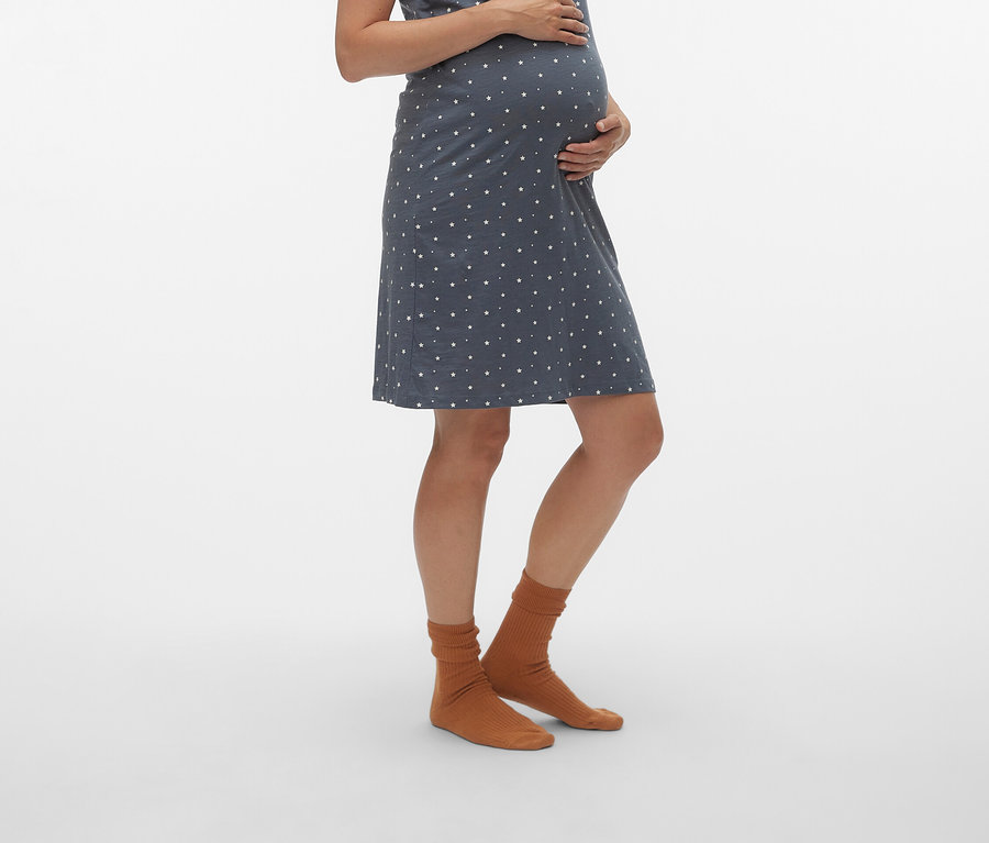 Tehotná žena nosí modré tehotenské šaty s bielymi bodkami a hnedé ponožky.