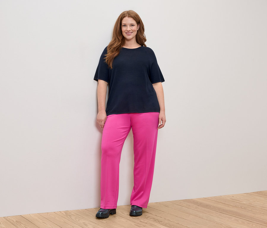 Žena s dlhými ryšavými vlasmi v tmavomodrom tričku a ružových nohaviciach.