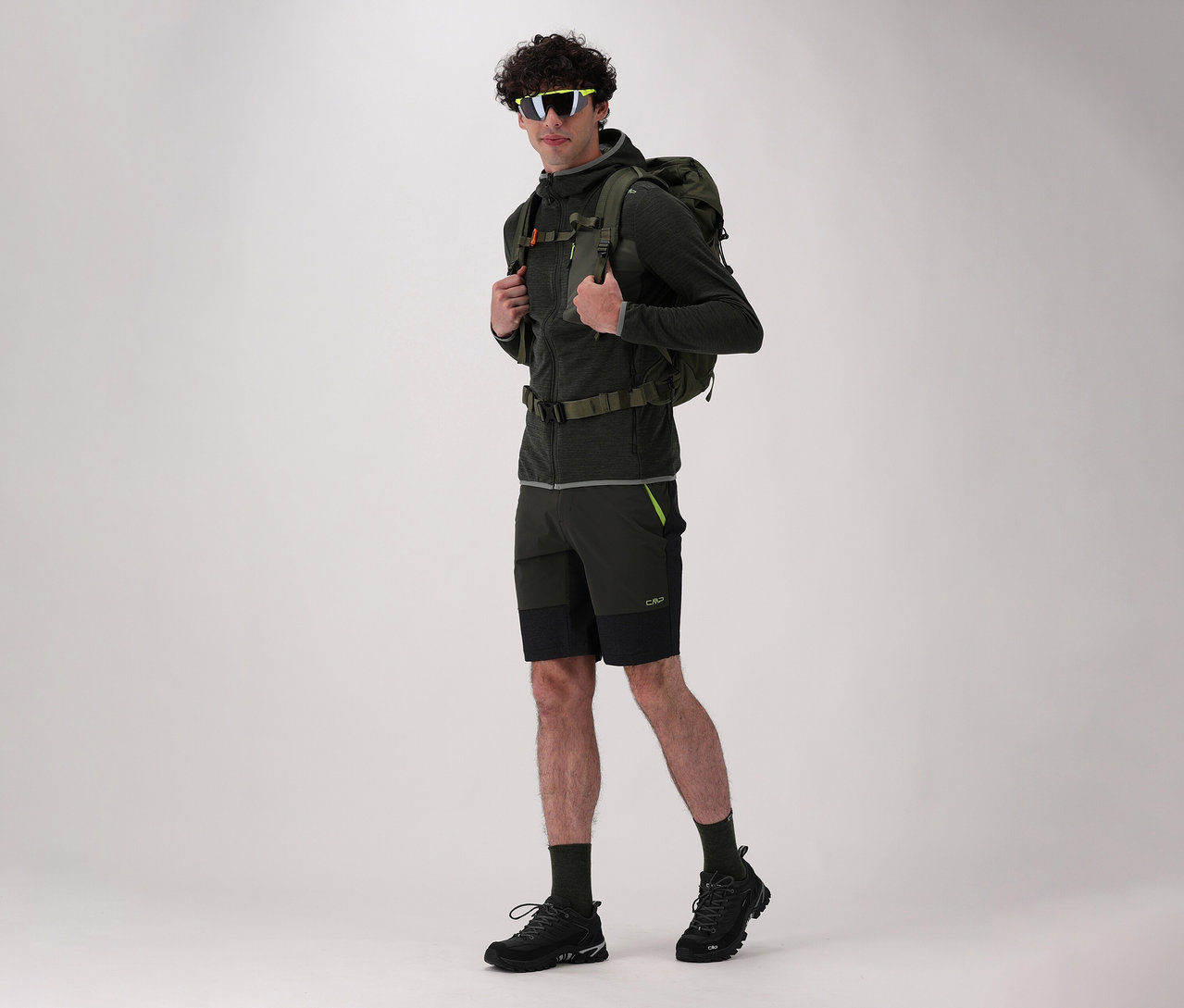 Muž s batohom a v čiernych trekingových topánkach CMP RIGEL LOW 2.0 WP pózuje na svetlom pozadí.