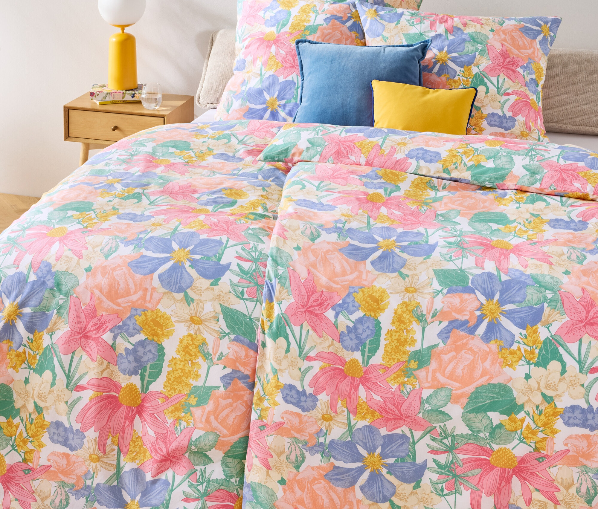 Kvetinová posteľná bielizeň Renforcé, dvojitá, štandardná a nadmerná veľkosť na posteli s modrými a žltými vankúšmi.