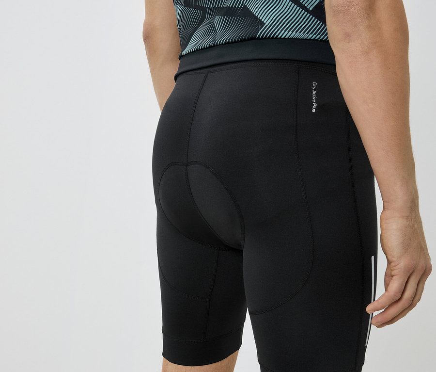 Detailný záber na zadnú časť osoby v čiernych cyklistických šortkách a modrozelenom tričku.