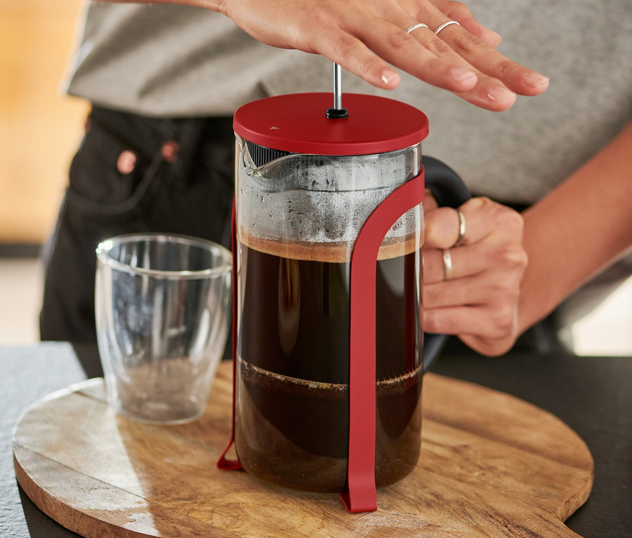 Žena stláča červenú kanvicu french press 800 ml na 6 šálok na drevenej doske.