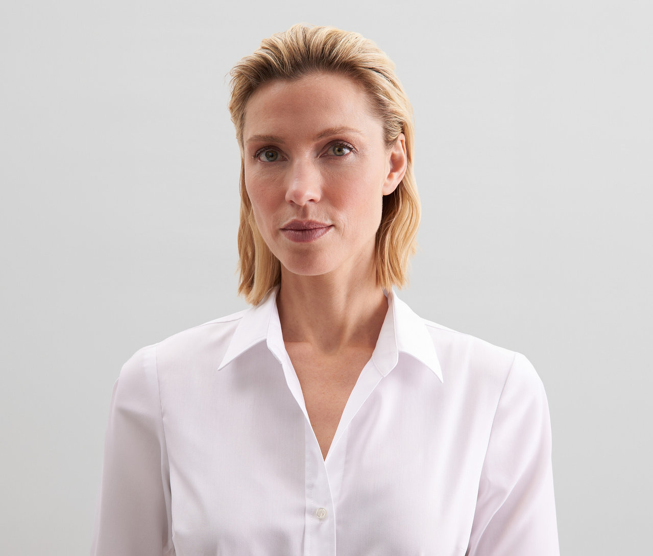 Žena s blond vlasmi má na sebe bielu blúzku Seidensticker Slim Fit non iron.