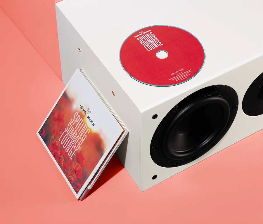 Červené CD a obal albumu »Best of Blank & Jones: Spring Summer Lounge« opreté o biely reproduktor.