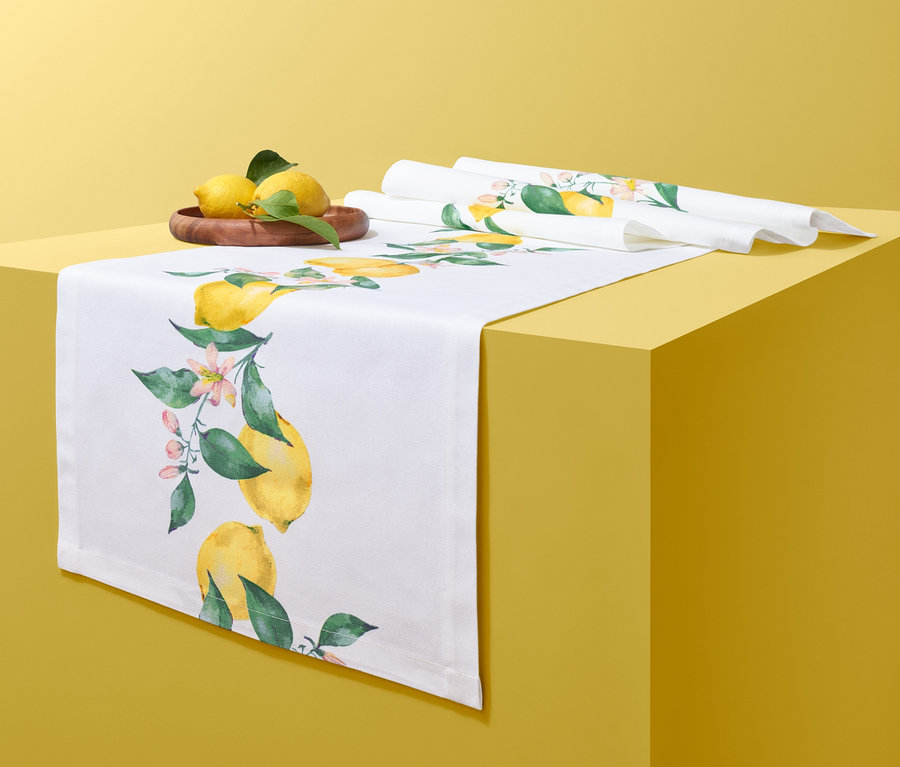 Na žltom stole leží biely behúň so vzorom citrónov, drevená miska s citrónmi a zrolovaný behúň.