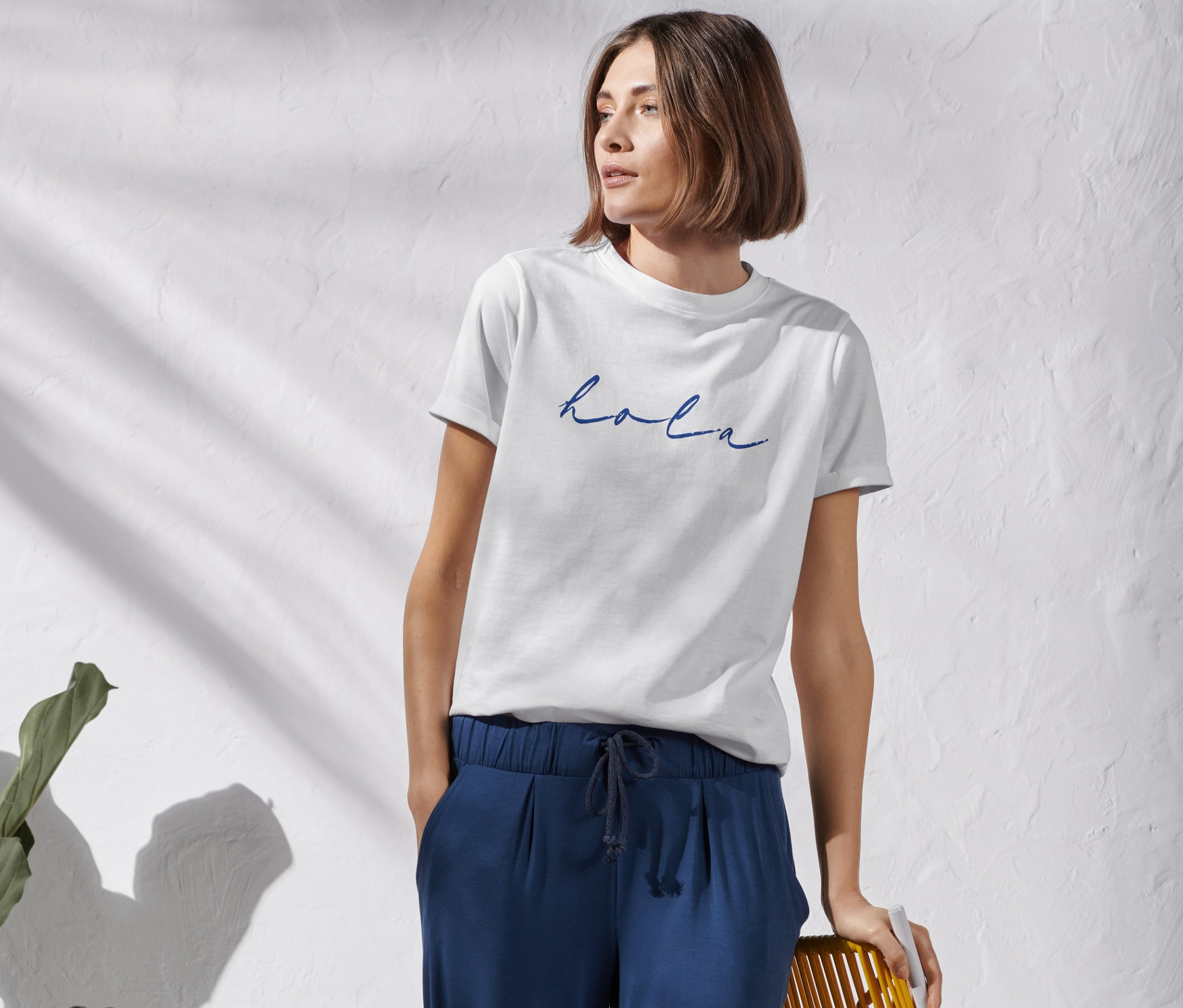 Žena stojí a má na sebe biele tričko s potlačou a modré nohavice.