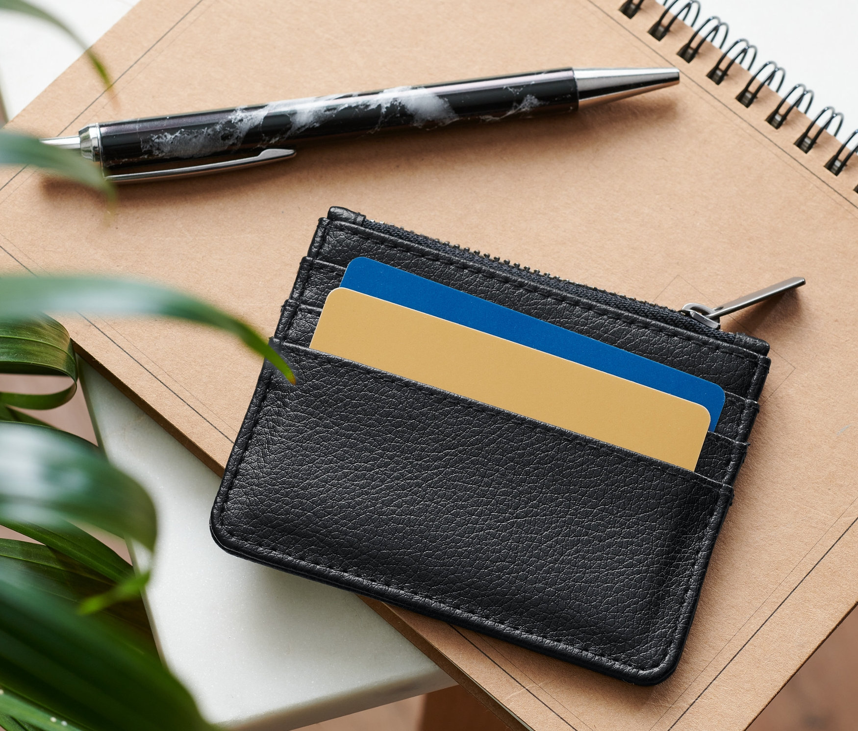 Čierne puzdro na platobné karty leží na poznámkovom bloku vedľa pera.
